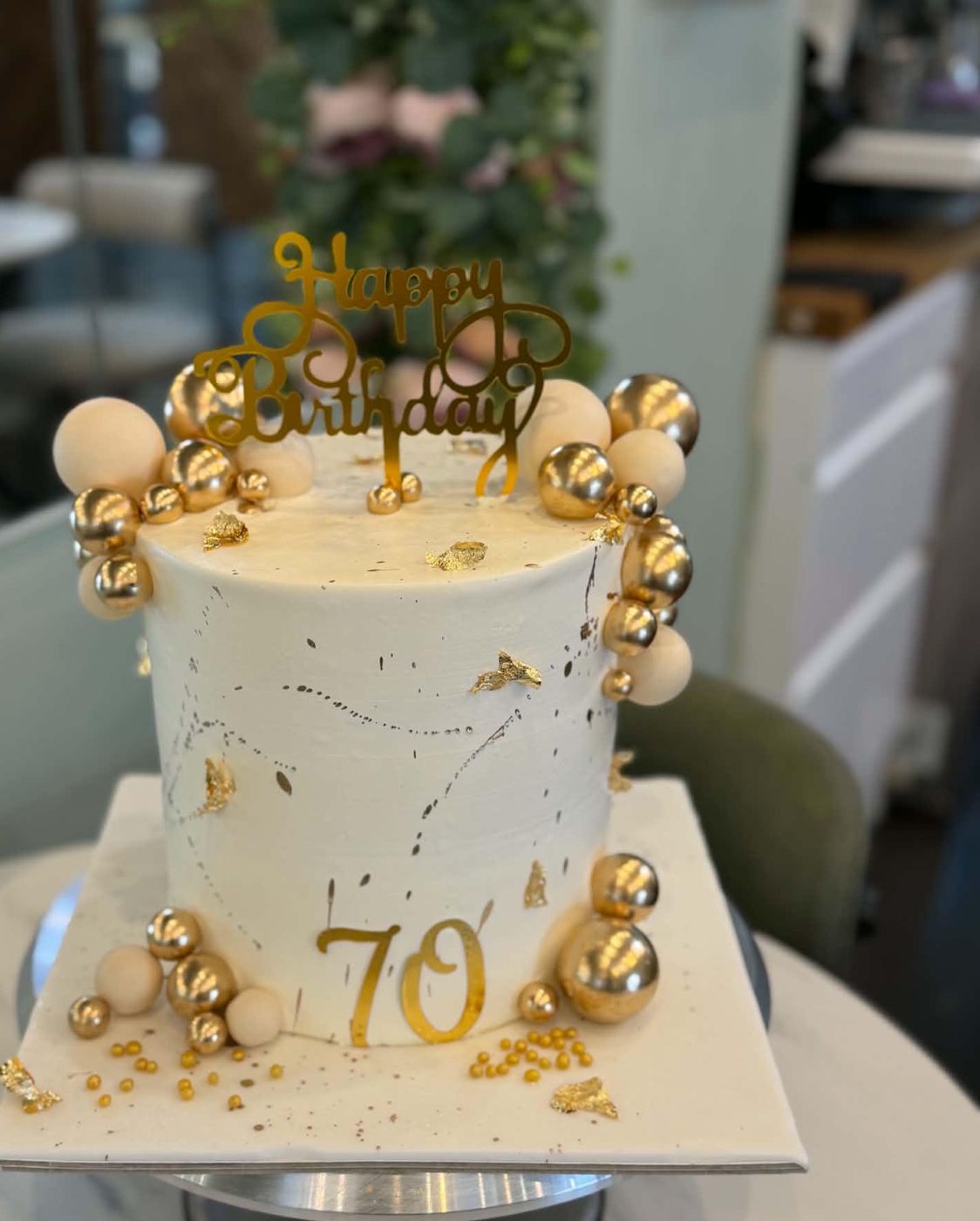 Tall white birthday cake with gold spheres and gold leaf