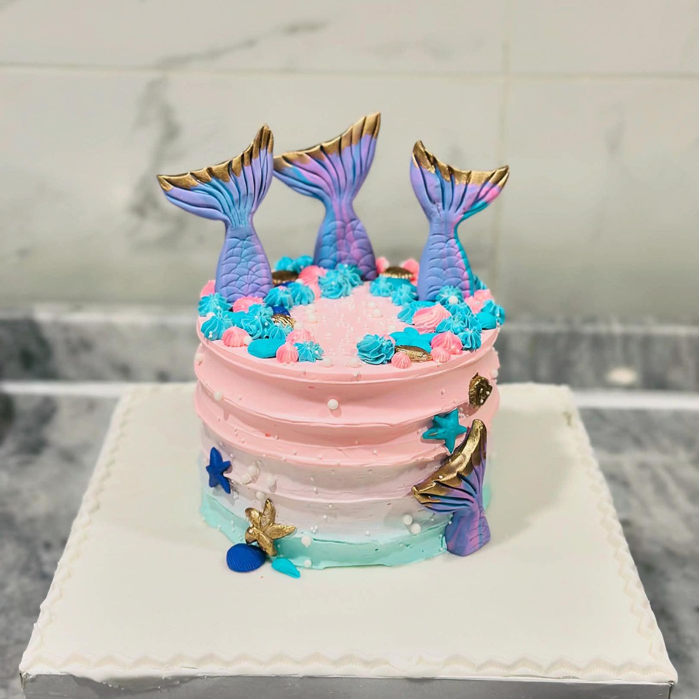 Pink and turquoise cake with three mermaid tails painted gold