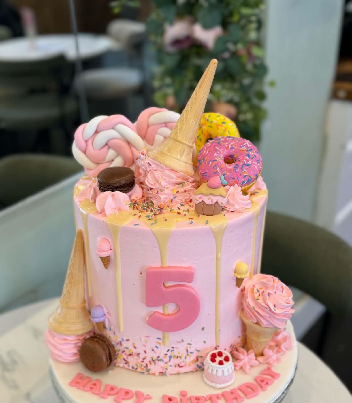 Pink drip cake with ice cream cones, macarons and doughnuts