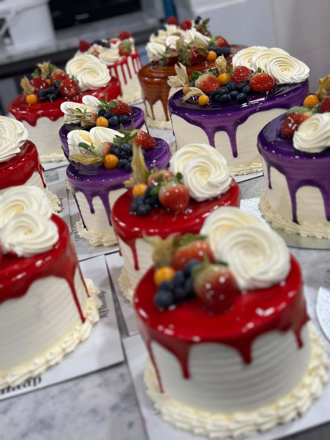 Drip cakes with red and purple glaze, cream rosettes and fresh berries