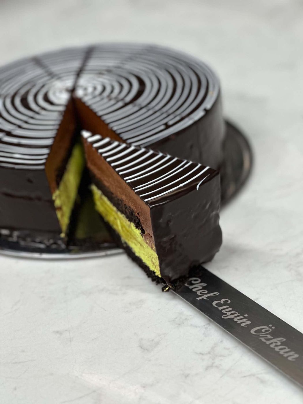 A slice of chocolate and pistachio mousse cake lifted from the whole cake